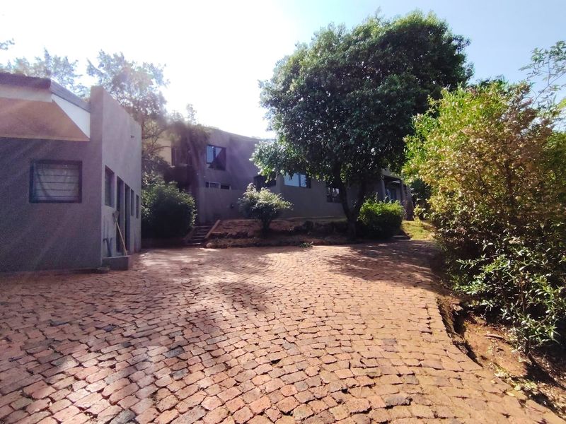 A view of the property exterior featuring a cobblestone driveway leading to the main building structure with concrete walls and casement windows.