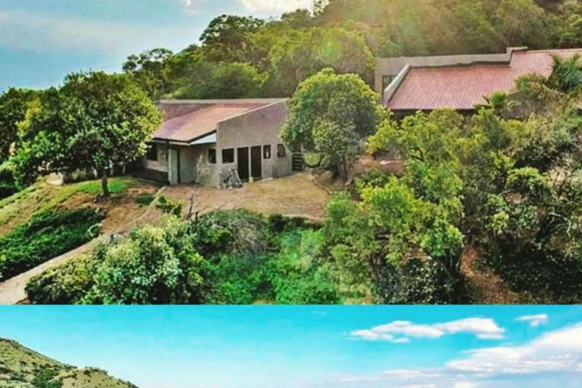 An aerial view of the farm property featuring multiple structures nestled into the hillside, surrounded by extensive natural landscape and mountain views.