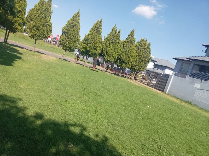 A well-maintained green lawn area featuring mature trees and a perimeter fence, providing a pleasant outdoor space.