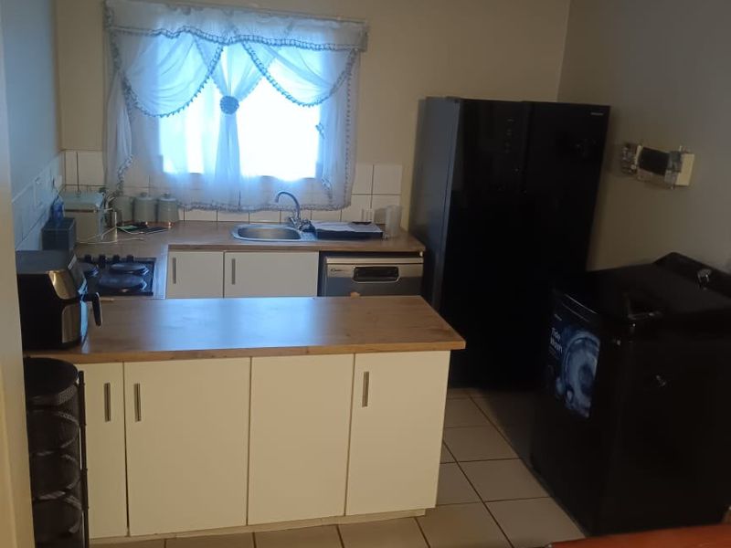 A functional kitchen featuring white cabinetry, laminate countertops, a stainless steel sink, and ceramic tile flooring, providing a practical workspace.