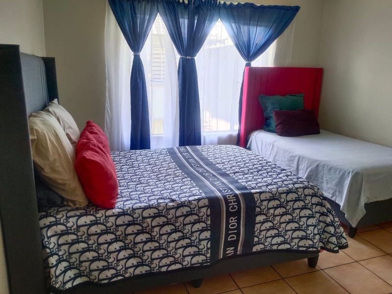 A bedroom featuring tiled flooring and large windows with curtains, providing natural light to the space.