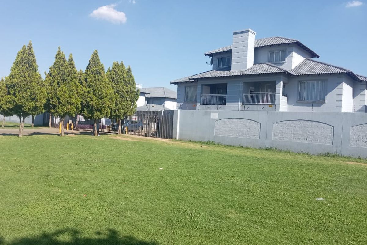 Front exterior view of a two-story residential house featuring a tiled roof, balcony with metal railings, and a secure perimeter wall with electric fencing.