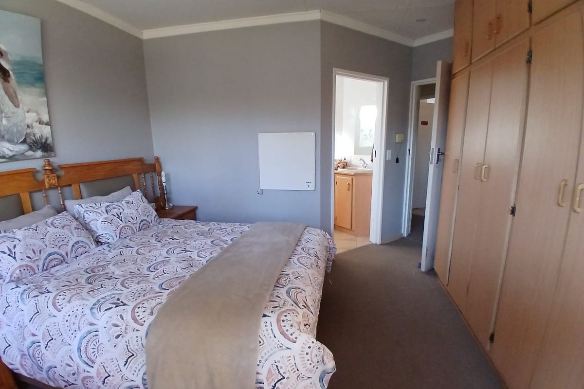 A bedroom featuring built-in wooden cupboards, neutral wall tones, carpeted flooring, and direct access to an en-suite bathroom.