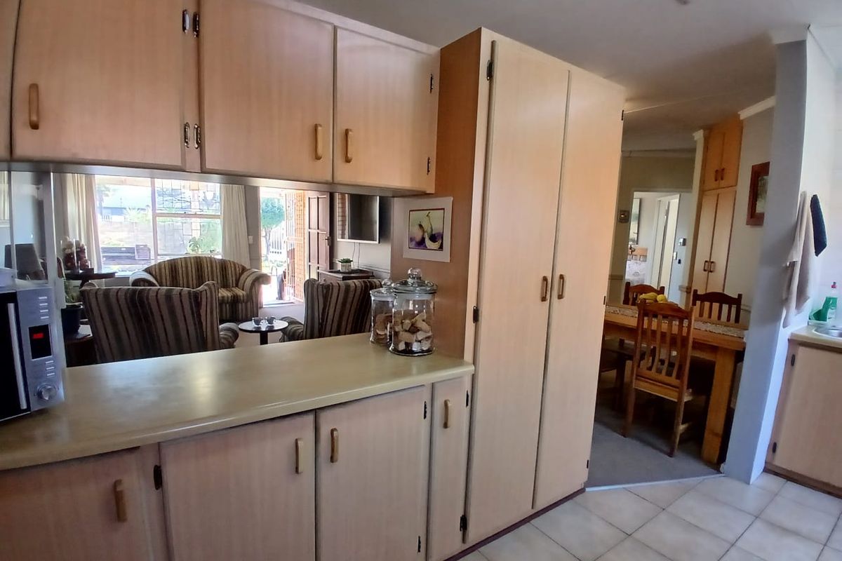 A functional kitchen featuring light-toned laminate cabinetry, ample storage space, and tiled flooring, with an open-plan layout connecting to the dining and living areas.