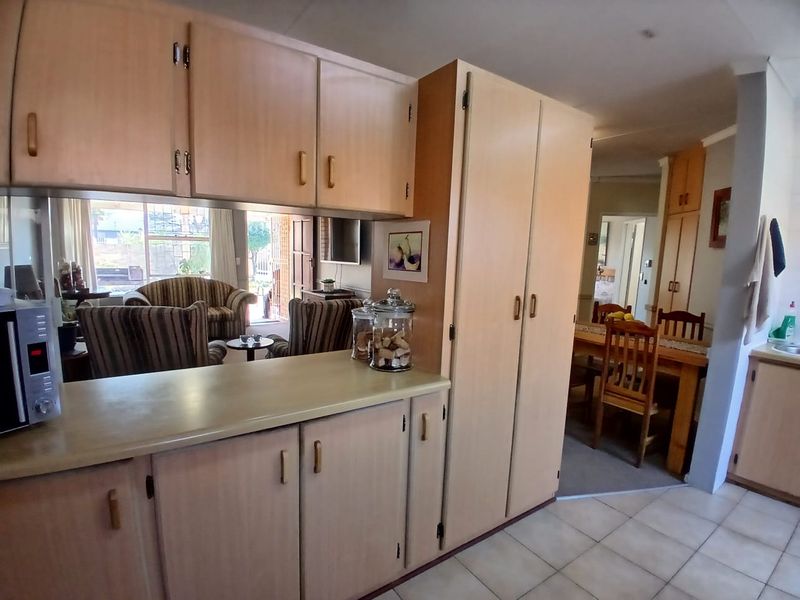 A functional kitchen featuring light-toned laminate cabinetry, ample storage space, and tiled flooring, with an open-plan layout connecting to the dining and living areas.