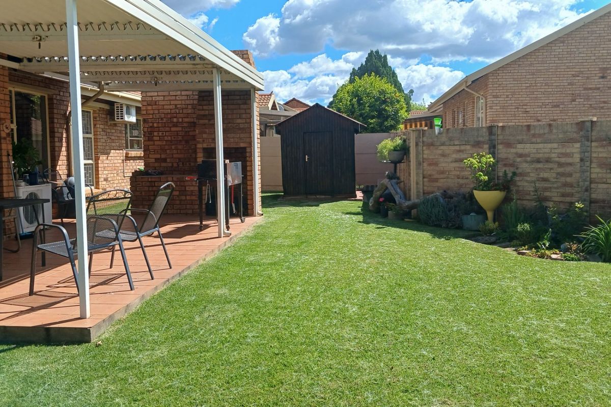 A private rear garden featuring a covered patio with a built-in braai, a well-maintained lawn, and a detached storage shed.