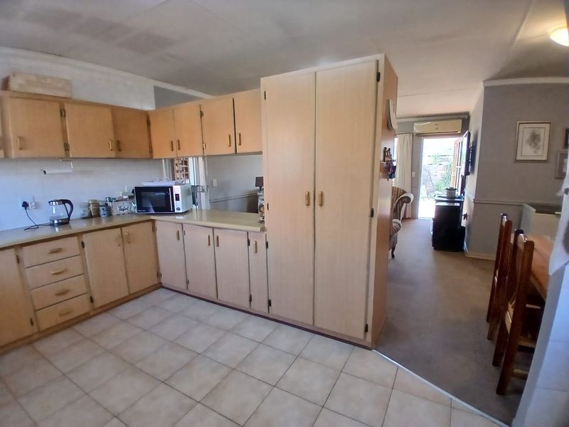 Open-plan kitchen and living area featuring light wood cabinetry, tiled kitchen flooring, and carpeted living space with access to the rear patio.