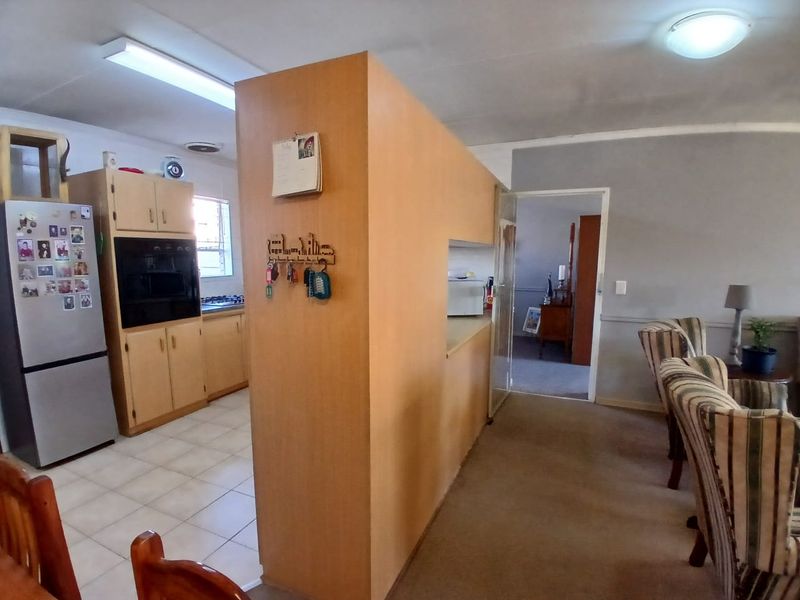 Open plan kitchen and living area featuring dated cabinetry, built-in oven, hob, and a central partition wall separating the kitchen from the living space.