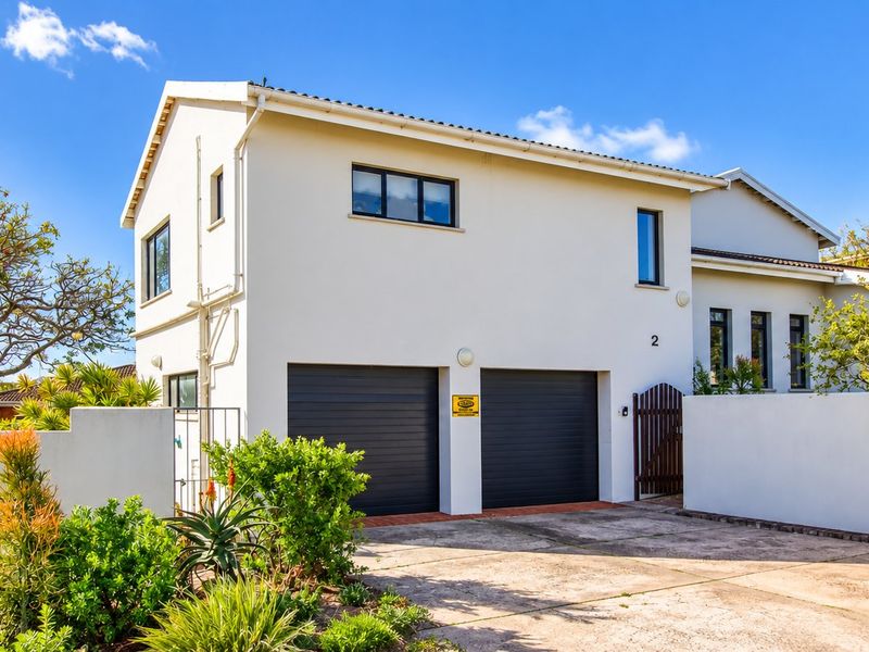 Front elevation of a two-story residential property featuring a double garage, concrete driveway, and secure boundary wall with a pedestrian gate.