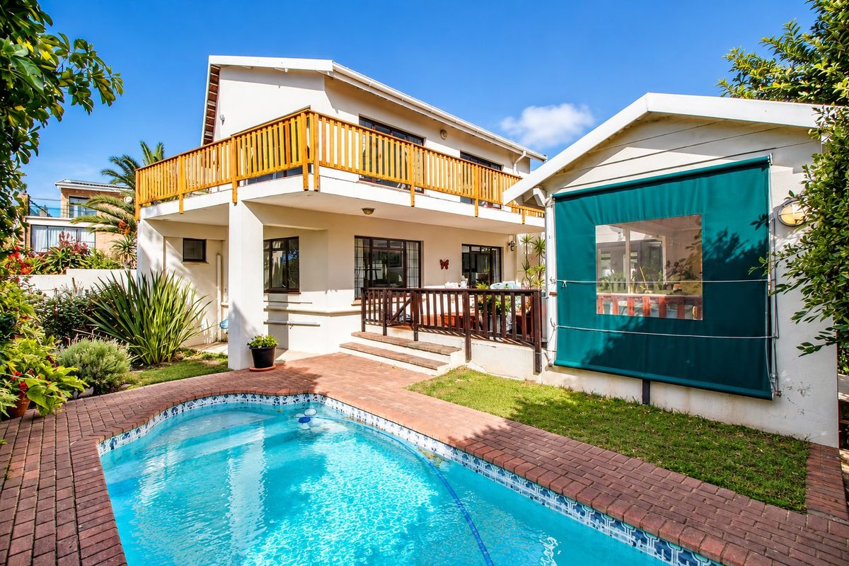 Rear exterior view featuring a swimming pool with brick surround, a raised wooden balcony, and a covered patio area with an outdoor roller blind.