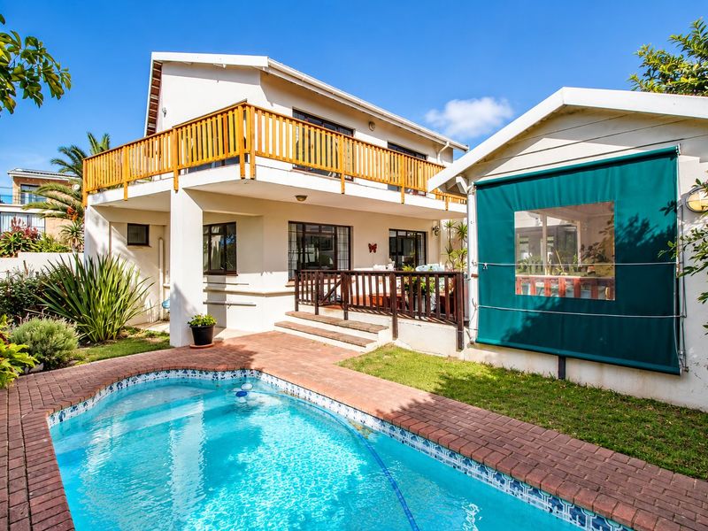 Rear exterior view featuring a swimming pool with brick surround, a raised wooden balcony, and a covered patio area with an outdoor roller blind.