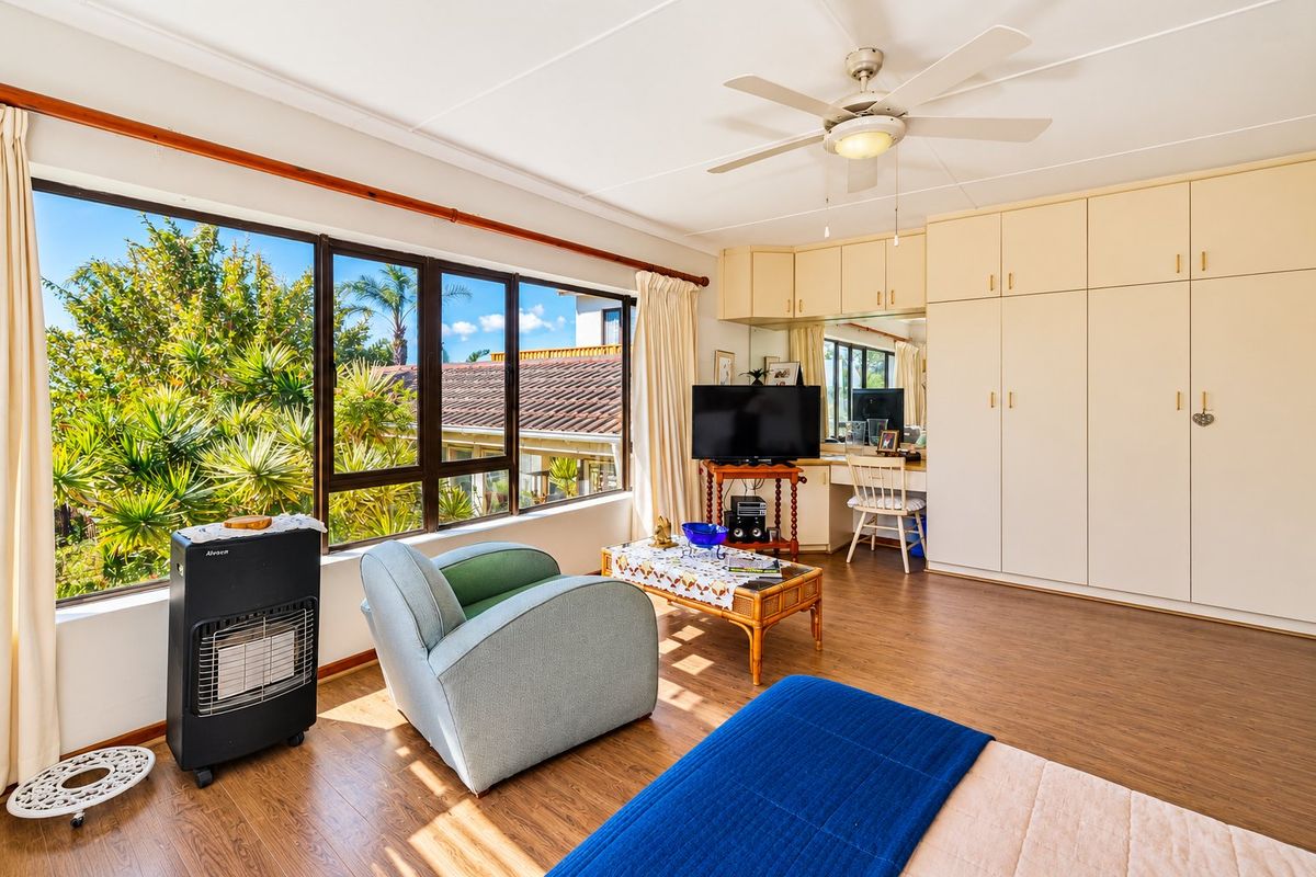 Spacious bedroom featuring extensive built-in cabinetry, laminate flooring, and a ceiling fan, with large windows providing ample natural light and garden views.