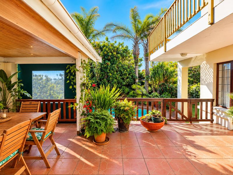 A spacious covered patio featuring tiled flooring, timber ceiling with recessed lighting, and a timber balustrade overlooking the garden and pool area.