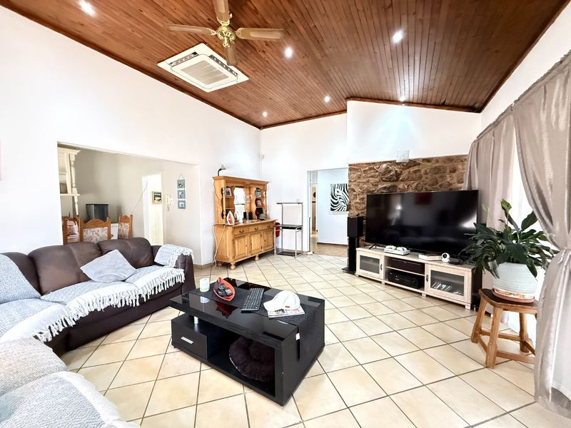 Spacious living room featuring a vaulted timber-clad ceiling, stone feature wall, and neutral ceramic floor tiles, offering a warm and inviting atmosphere.