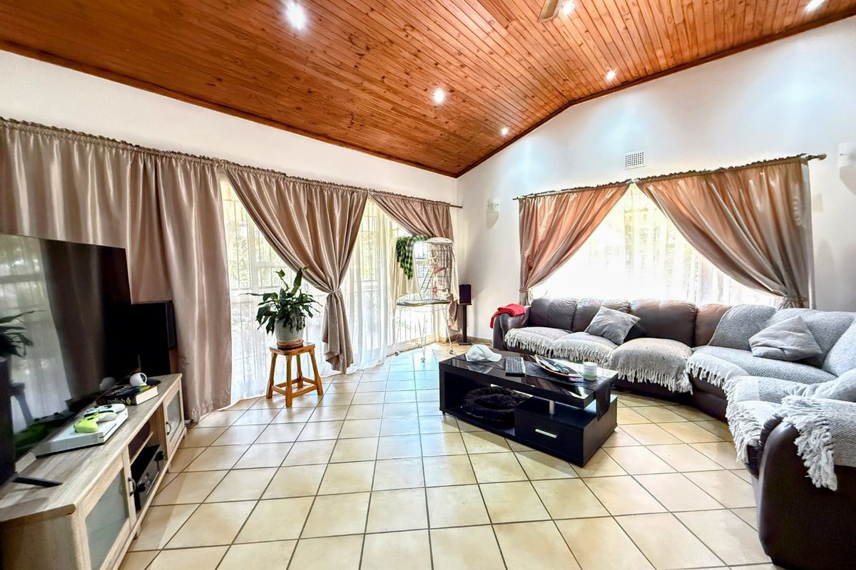 Spacious living room featuring a vaulted timber ceiling, tiled flooring, and large sliding glass doors providing ample natural light.