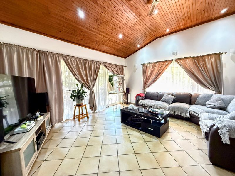 Spacious living room featuring a vaulted timber ceiling, tiled flooring, and large sliding glass doors providing ample natural light.