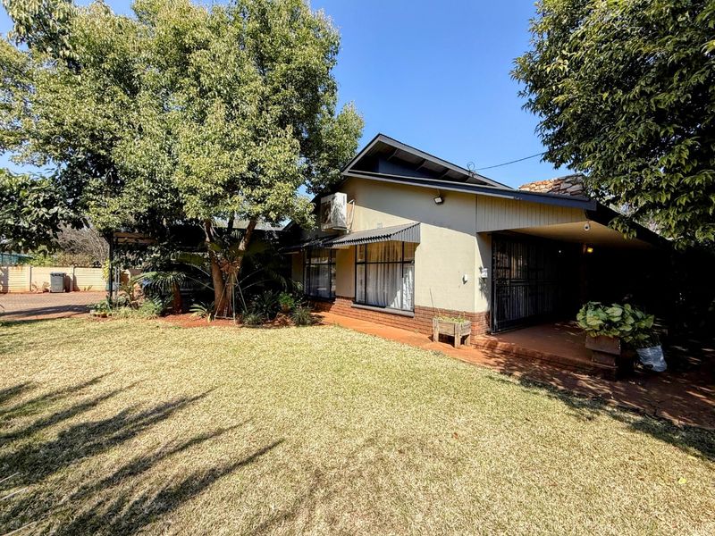 A rear view of the house featuring a covered patio area, established garden, and brick exterior finishes.