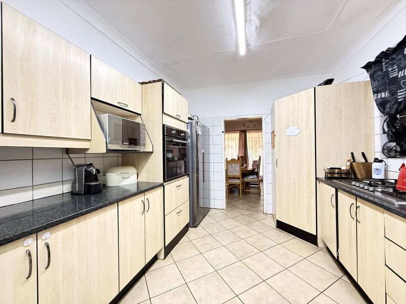 A functional kitchen featuring light wood-finish cabinetry, dark laminate countertops, built-in oven and microwave, gas hob, and tiled flooring.