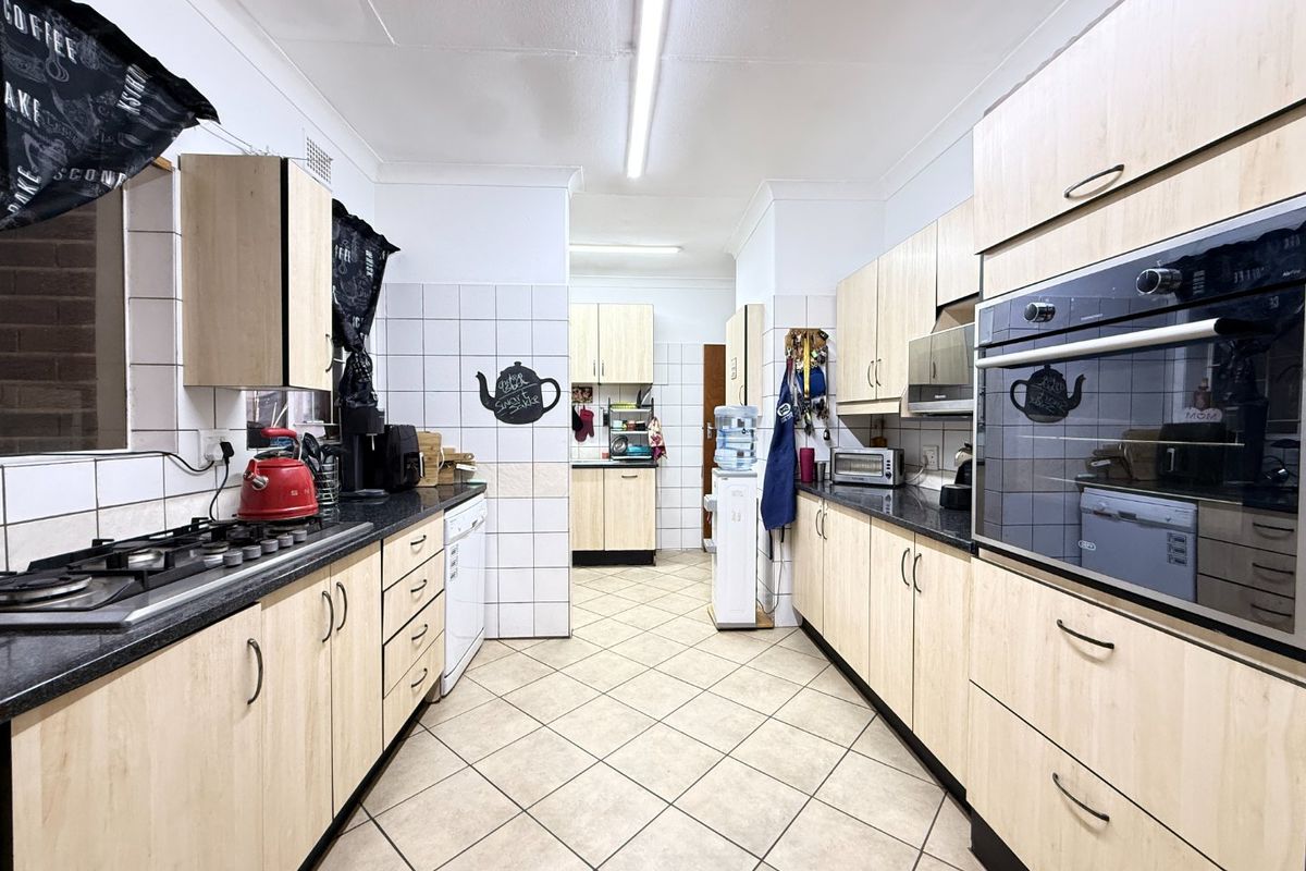 A functional galley-style kitchen featuring light wood-finish cabinetry, dark countertops, a gas hob, and a built-in oven with tiled flooring and backsplash.