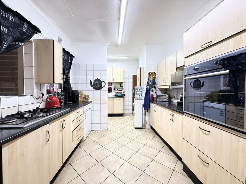 A functional galley-style kitchen featuring light wood-finish cabinetry, dark countertops, a gas hob, and a built-in oven with tiled flooring and backsplash.