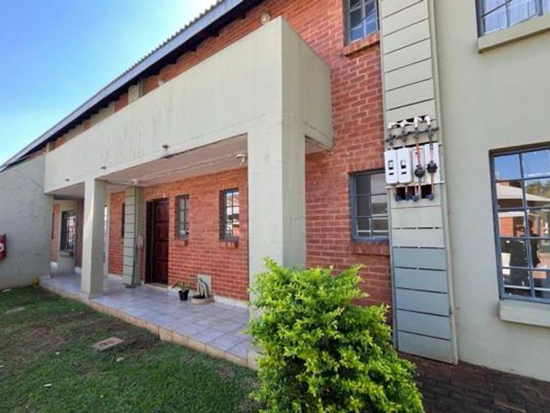 Front exterior view of the apartment building featuring a covered tiled patio, brick facade, and external utility meters.