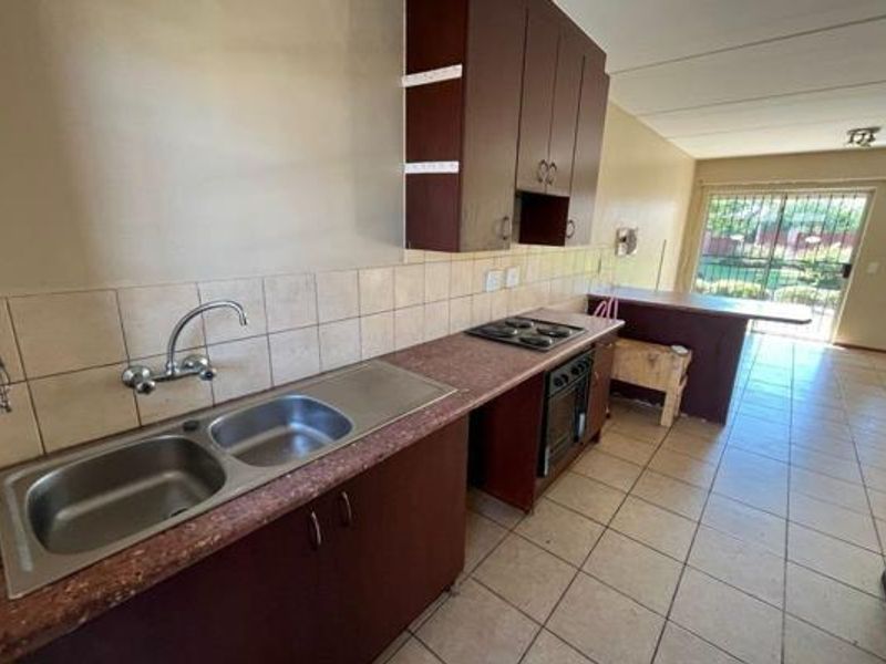 Open plan kitchen featuring built-in cabinetry, electric hob, oven, and double sink, flowing into a living area with access to the exterior.