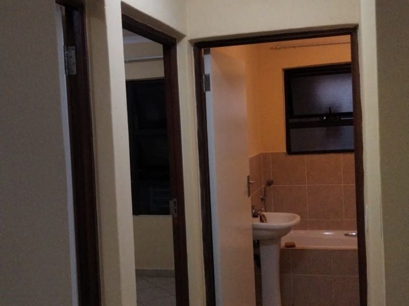 A functional hallway with tiled flooring and coved ceilings, providing access to adjacent rooms including a bathroom with a pedestal basin and bathtub.
