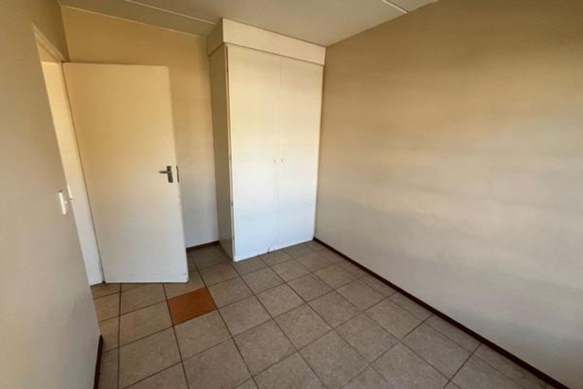 An empty bedroom featuring tiled flooring and a built-in wardrobe, requiring minor cosmetic updates to the walls and flooring.