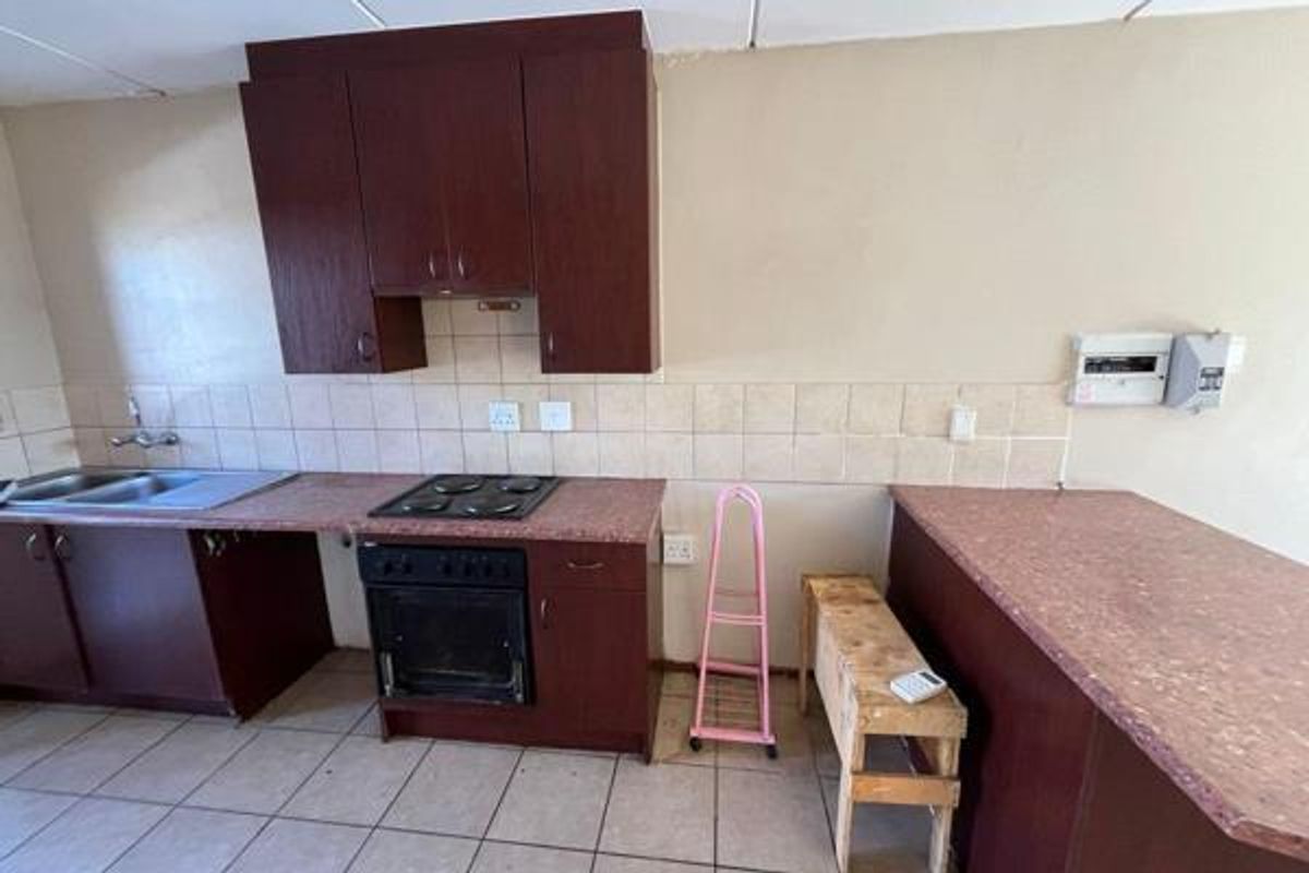 A functional kitchen featuring dark wood-look cabinetry, laminate countertops, a built-in oven and hob, and a double bowl sink with tiled splashback.