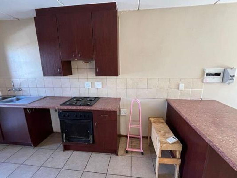 A functional kitchen featuring dark wood-look cabinetry, laminate countertops, a built-in oven and hob, and a double bowl sink with tiled splashback.
