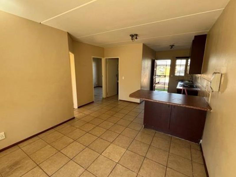 Open-plan living and kitchen area featuring tiled flooring, a breakfast bar, and built-in cabinetry, offering a functional layout ready for modernization.