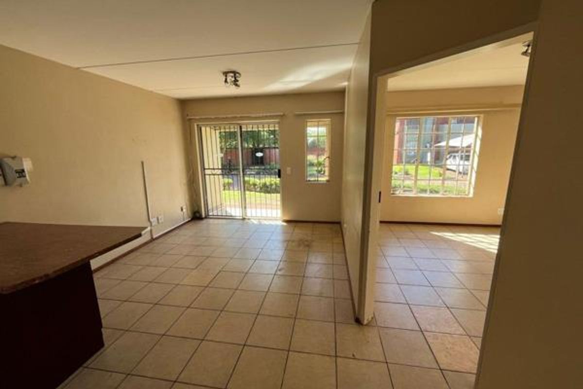 An empty, open-plan living area featuring tiled flooring, a breakfast bar, and a sliding glass door leading to an outdoor space.