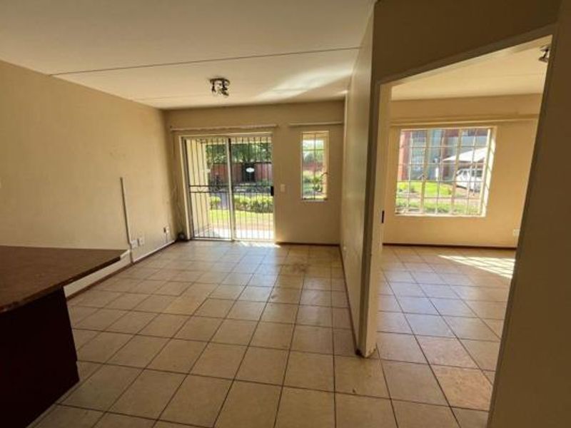 An empty, open-plan living area featuring tiled flooring, a breakfast bar, and a sliding glass door leading to an outdoor space.