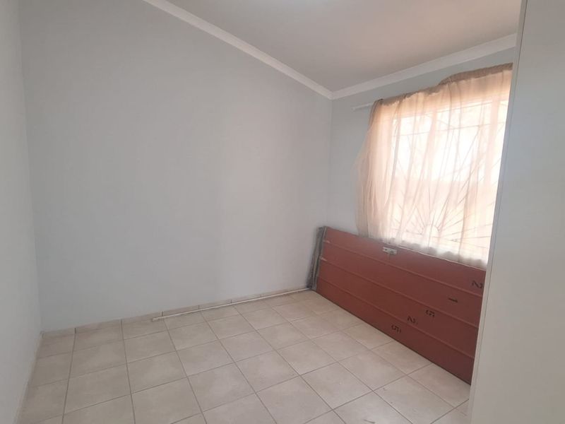 An empty bedroom featuring tiled flooring, coved ceilings, and a window fitted with security bars.