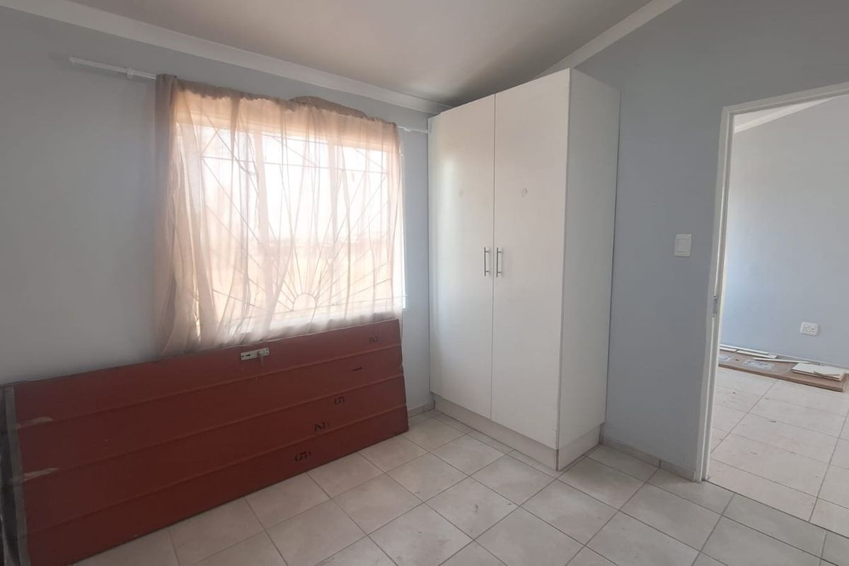A functional bedroom featuring tiled flooring, a built-in wardrobe, and a window fitted with a security gate.