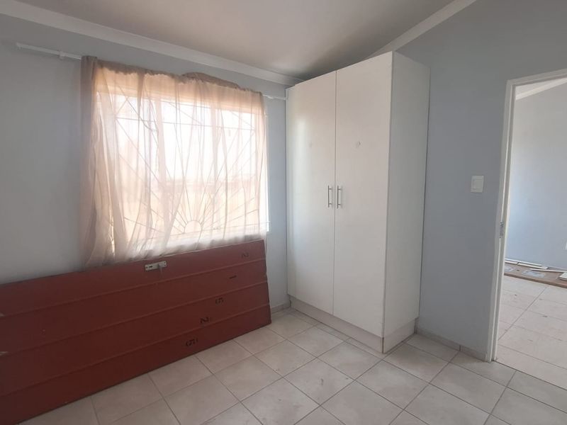 A functional bedroom featuring tiled flooring, a built-in wardrobe, and a window fitted with a security gate.