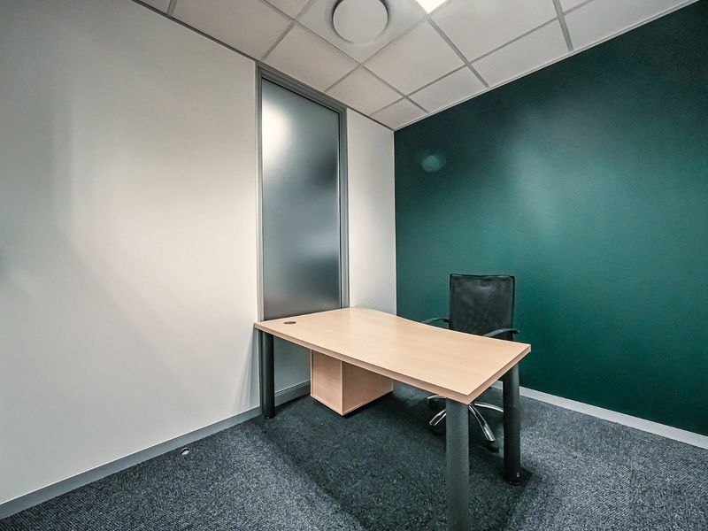 A compact, modern office space featuring a dark green accent wall, suspended ceiling, and frosted glass partition, providing a professional work environment.