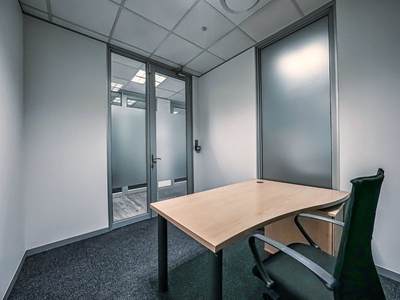 A professional office space featuring a suspended ceiling, carpeted flooring, and a glass partition with a frosted door for privacy.