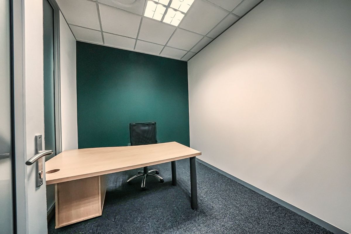 A clean, professional office space featuring a modern green accent wall, suspended ceiling with recessed lighting, and durable carpet flooring.