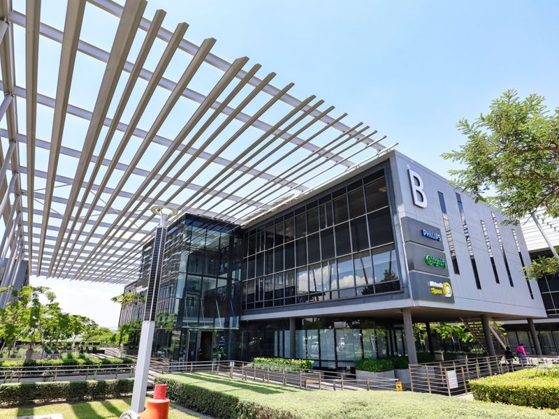 Modern commercial building facade featuring a prominent metal pergola, extensive glass curtain walling, and well-maintained landscaped grounds.
