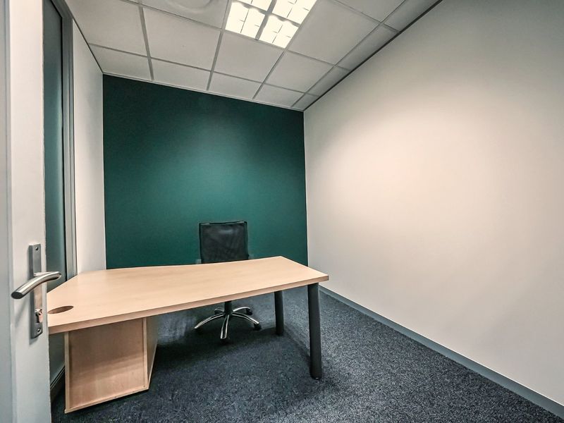 A clean, professional office space featuring a modern green accent wall, suspended ceiling with recessed lighting, and durable carpet flooring.