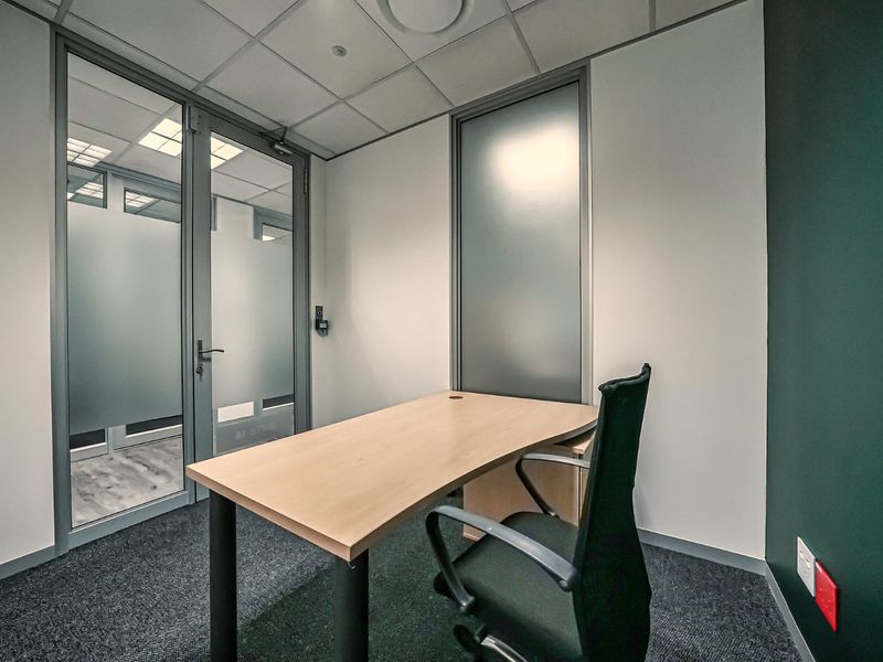 A professional commercial office space featuring a suspended ceiling, carpeted flooring, and a frosted glass partition for privacy.