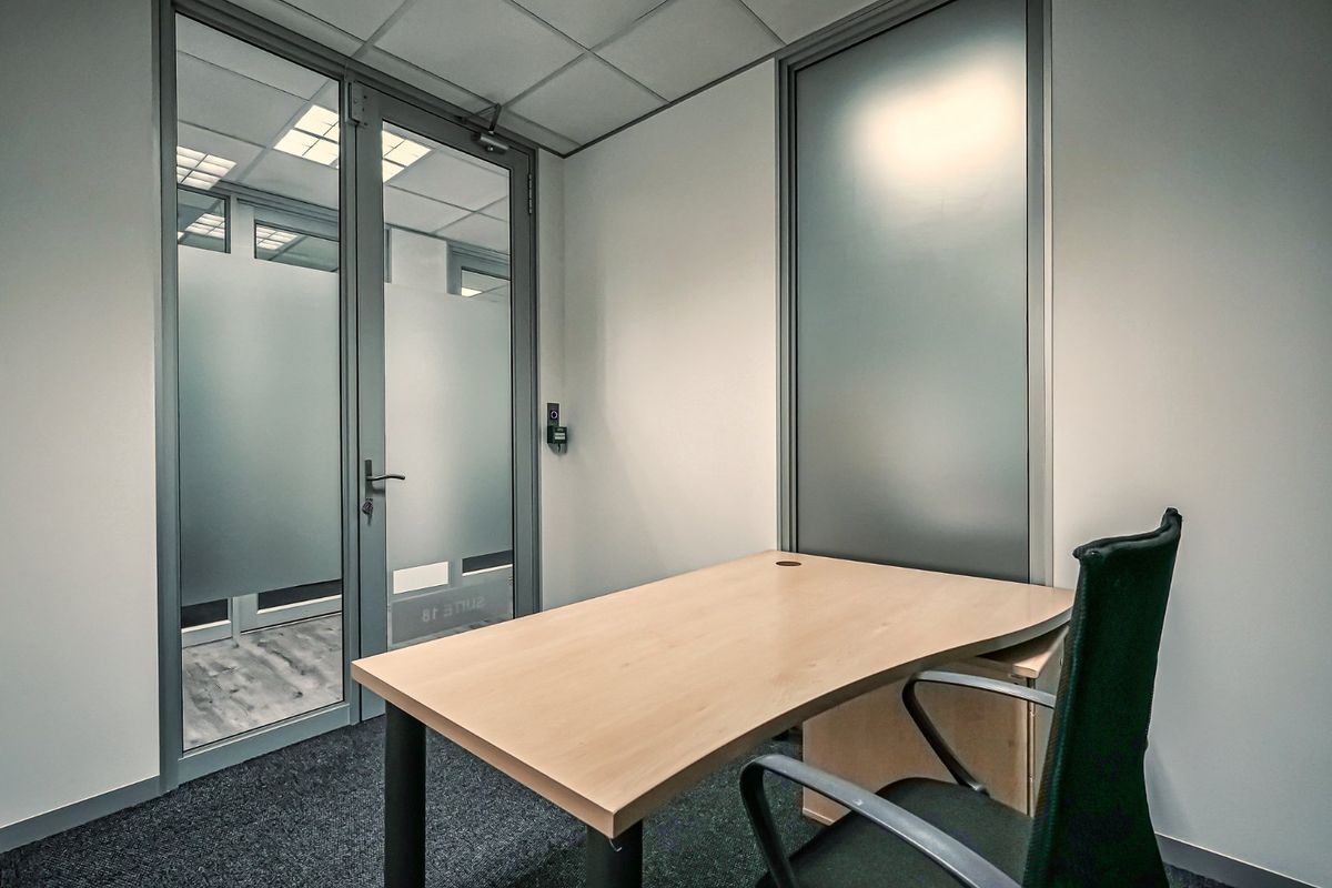 A professional office space featuring a suspended ceiling, carpeted flooring, and a modern frosted glass partition door.