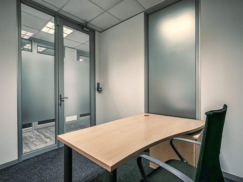 A professional office space featuring a suspended ceiling, carpeted flooring, and a modern frosted glass partition door.