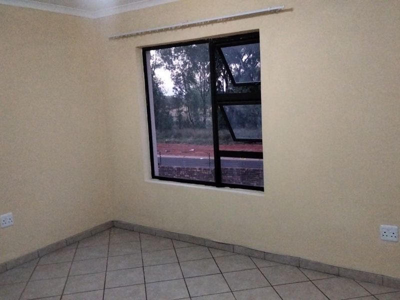 A clean, empty bedroom featuring neutral wall paint, tiled flooring, and a large aluminium-framed window providing natural light.