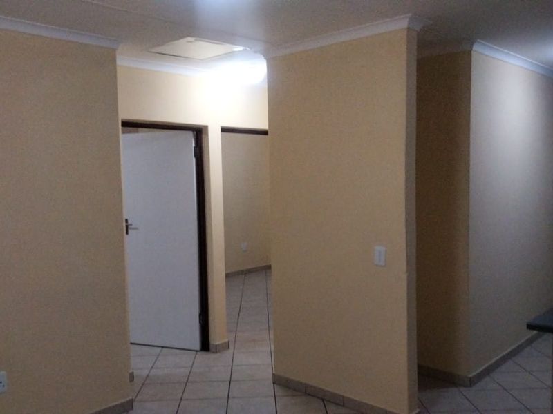 A functional, empty hallway featuring tiled flooring, neutral wall finishes, and access to multiple rooms within the property.