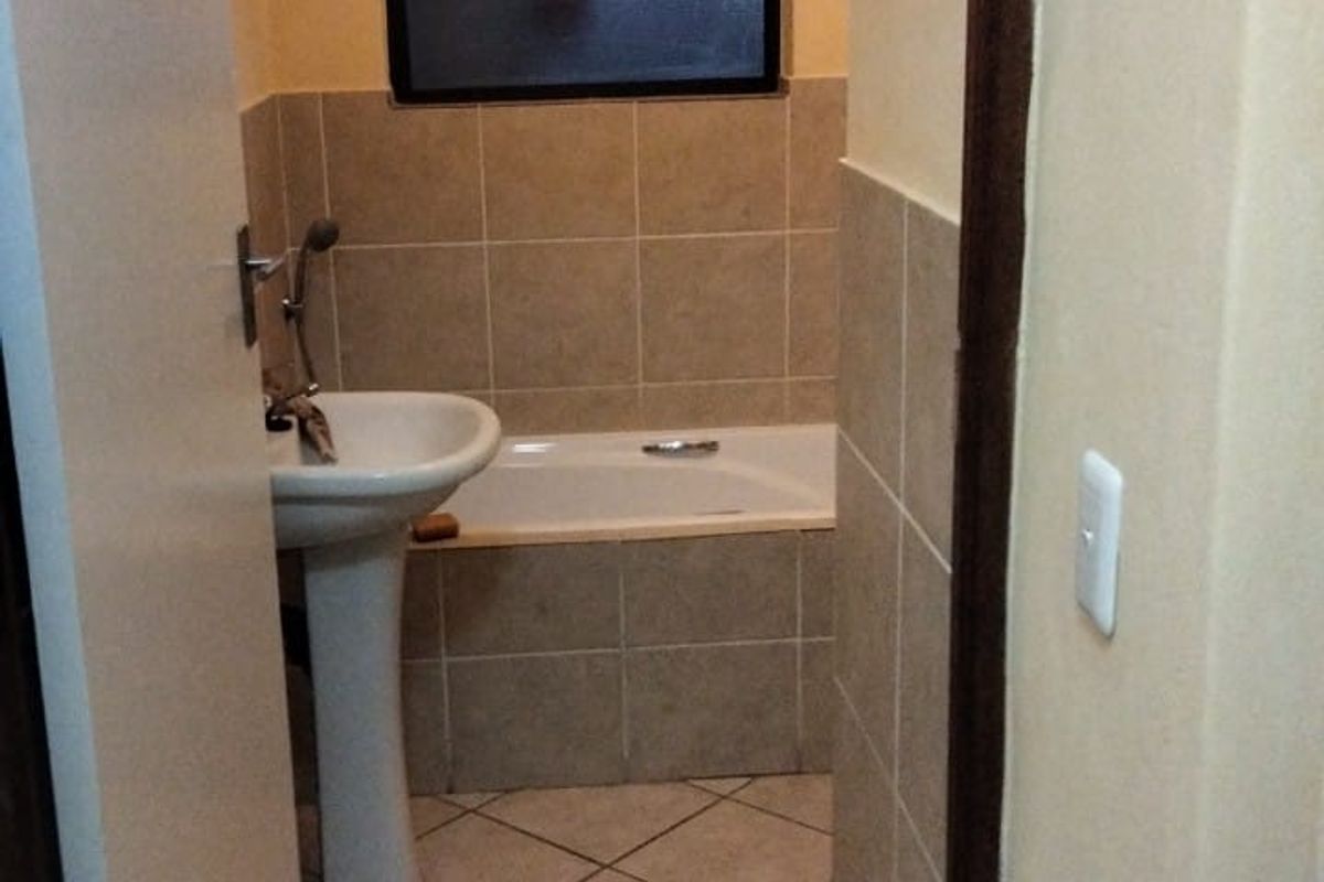 A functional bathroom featuring a pedestal basin, a built-in bathtub with tiled surround, and neutral floor tiling.