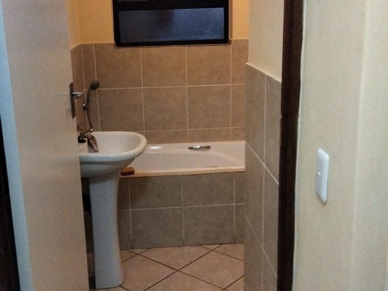A functional bathroom featuring a pedestal basin, a built-in bathtub with tiled surround, and neutral floor tiling.