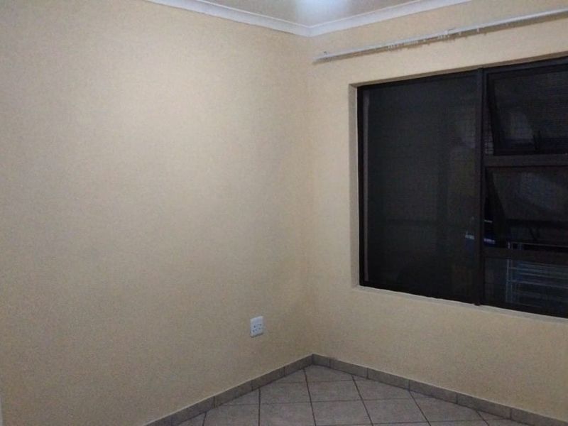 A clean, empty bedroom featuring neutral walls, tiled flooring, and an aluminium-framed window with a curtain track.