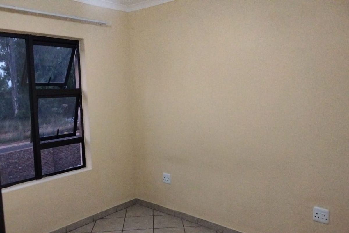 A clean, empty bedroom featuring neutral painted walls, tiled flooring, and a modern aluminium-framed window.